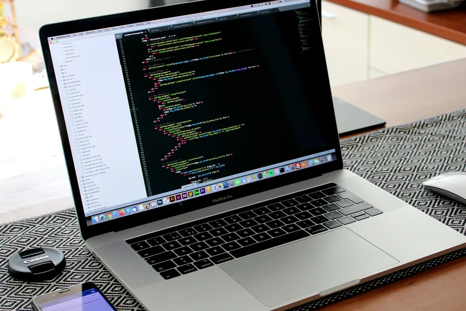 Ρεαλιστικό γραφείο με laptop που δείχνει κώδικα για μοντέρνα ιστοσελίδα iPixel, smartphone και αξεσουάρ, που αναδεικνύουν τις τάσεις AI, responsive design και UX/UI για το 2025.